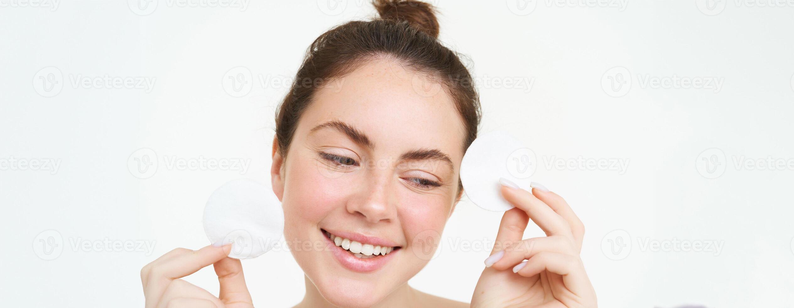 Beauty woman with clear glowing face, showing cotton cosmetic pads for makeup removal, cleansing her facial skin, standing over white background photo