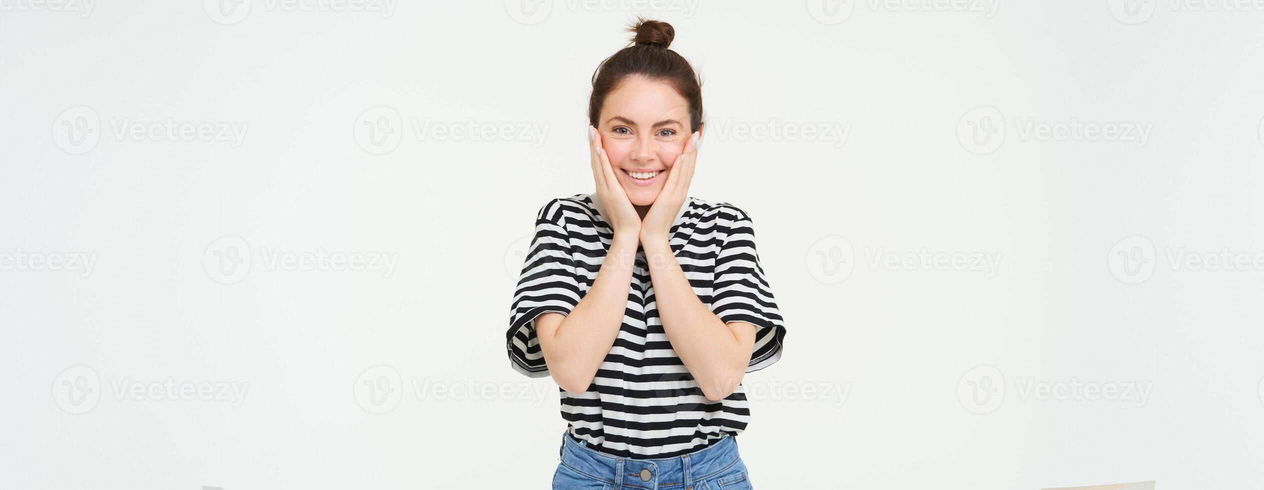 retrato de linda sonriente niña rubor, sostiene manos en las mejillas y mira entusiasmado, recibir contento noticias, soportes terminado blanco antecedentes foto