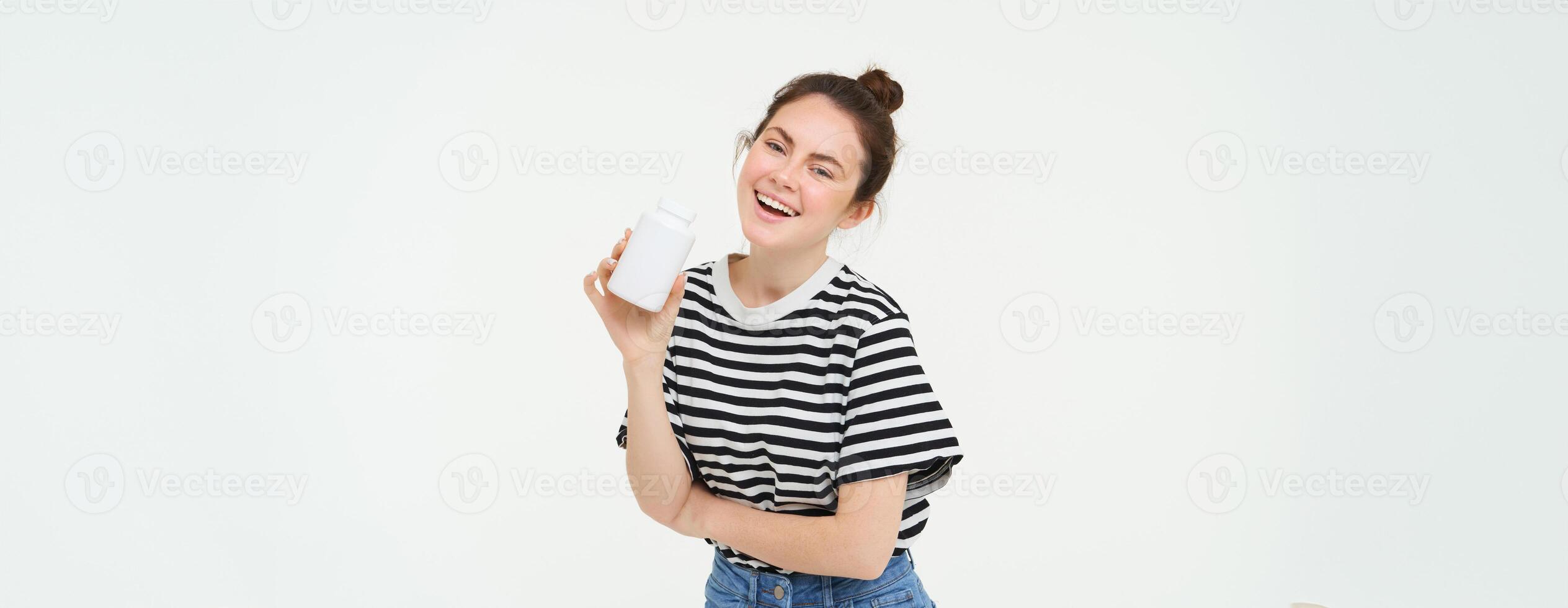 Healthcare and wellbeing. Young woman holding bottle with vitamins, dietary supplements, treatment for good skin and hair, standing over white background photo