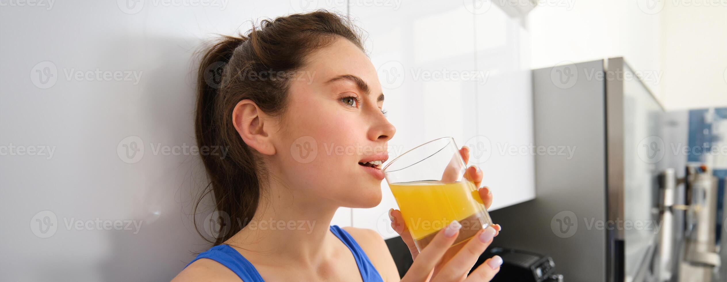 Beautiful woman drinking an organic orange juice. Fit young woman drinking from glass. Healthy girl enjoy detox drink and looking away photo