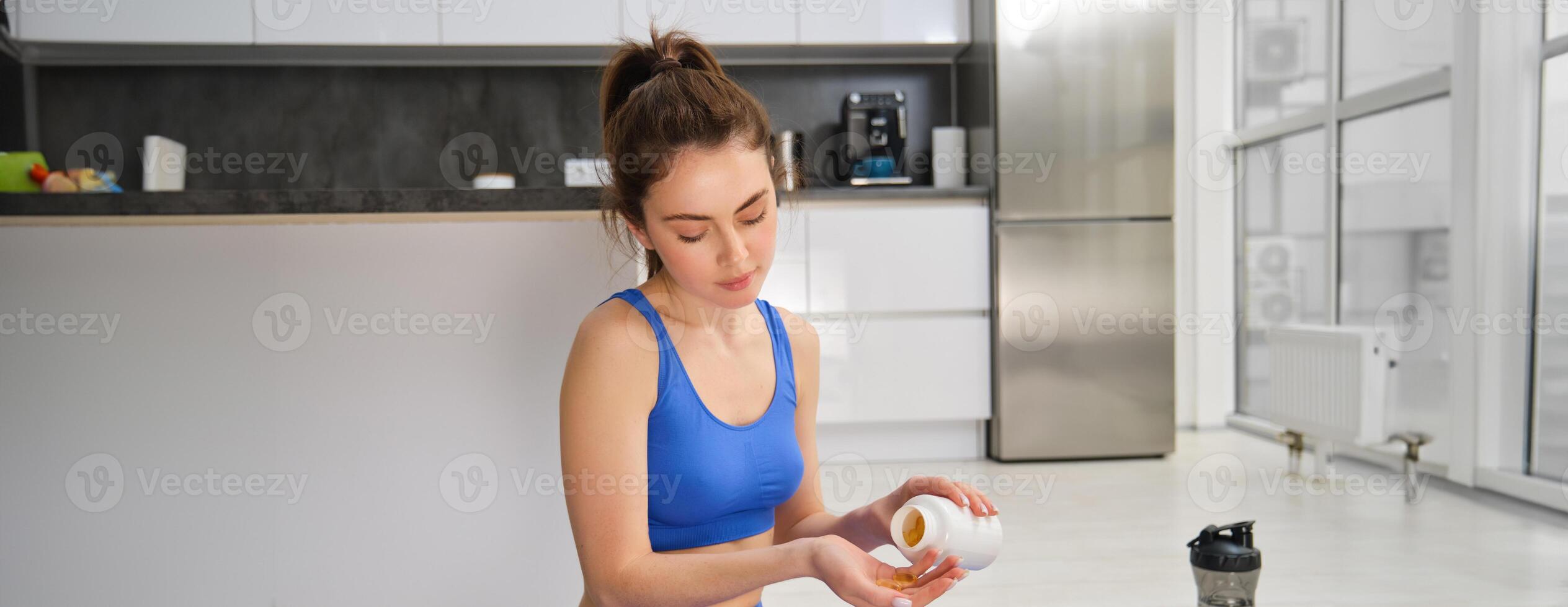 Portrait of beautiful and healthy fitness woman, taking vitamins, dietary supplements for muscles and bones, doing workout training at home photo