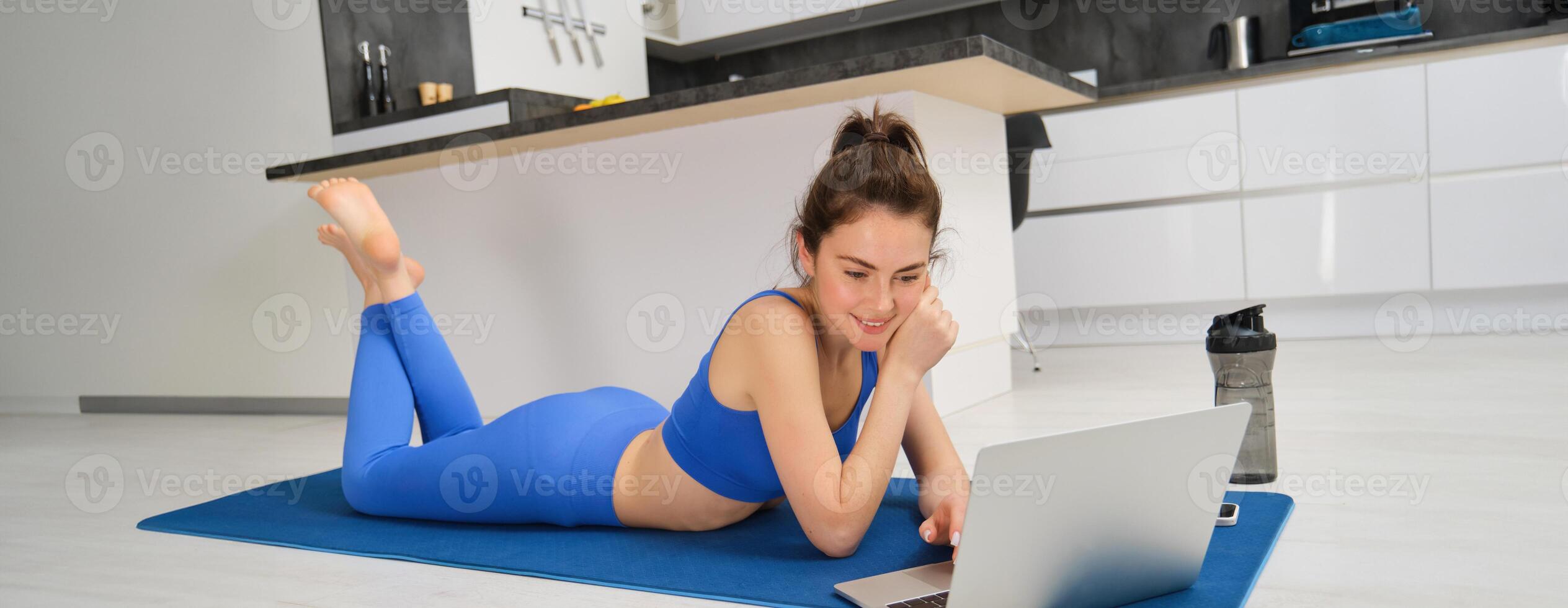 retrato de joven aptitud mujer, tendido en caucho estera, utilizando computadora portátil, mirando para rutina de ejercicio vídeo tutoriales en línea foto