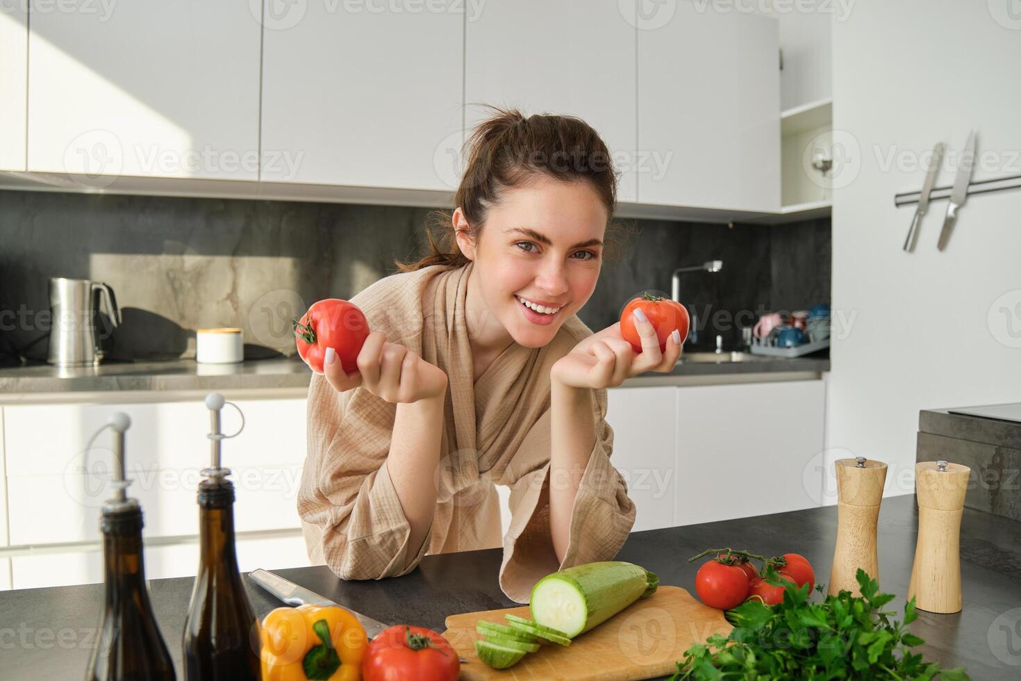 Portrait of woman cooking at home in the kitchen, holding tomatoes, preparing delicious fresh meal with vegetables, standing near chopping board photo