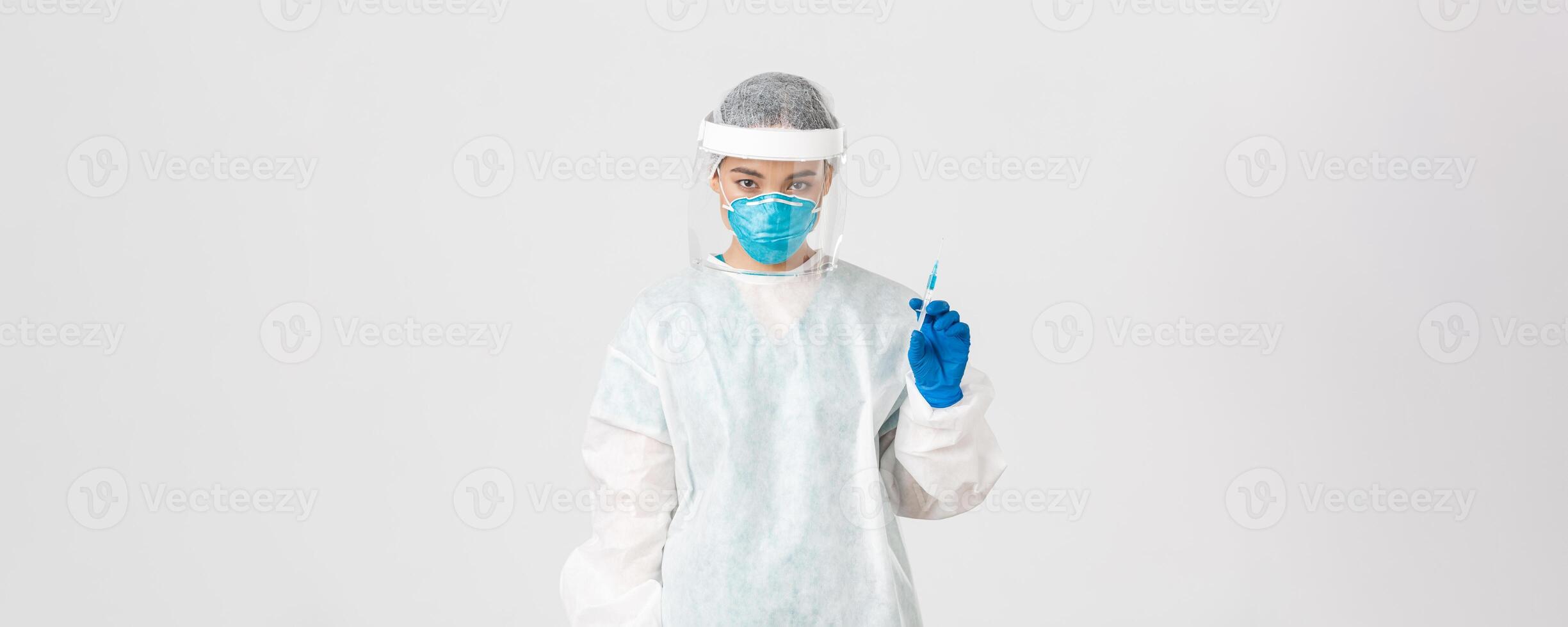 Covid-19, coronavirus disease, healthcare workers concept. Serious-looking confident asian female doctor in medical respirator and personal protective equipment, holding syringe with vaccine photo