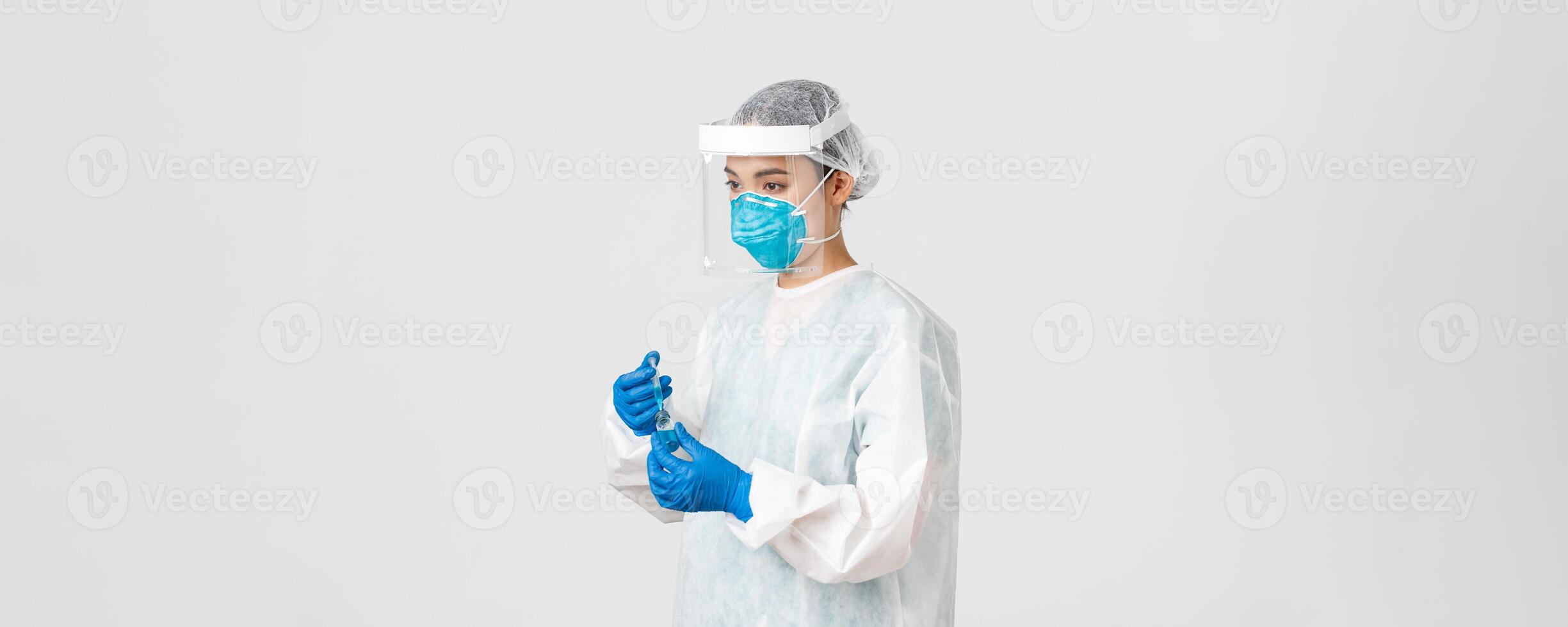 Covid-19, coronavirus disease, healthcare workers concept. Side view of serious young asian female doctor, physician in personal protective equipment insert syringe into ampoule with vaccine photo