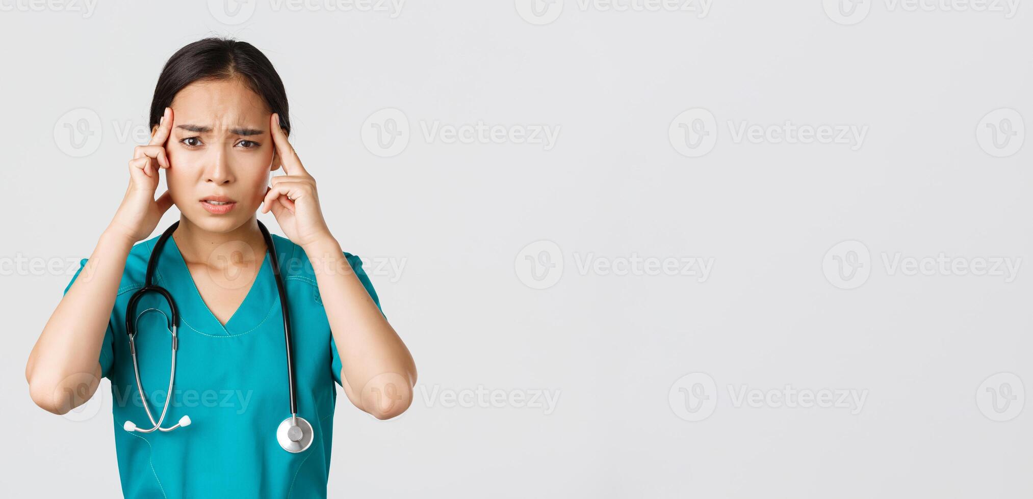 Healthcare workers, preventing virus, quarantine campaign concept. Exhausted asian female doctor feeling dizzy, touching head and grimacing from headache, standing white background photo
