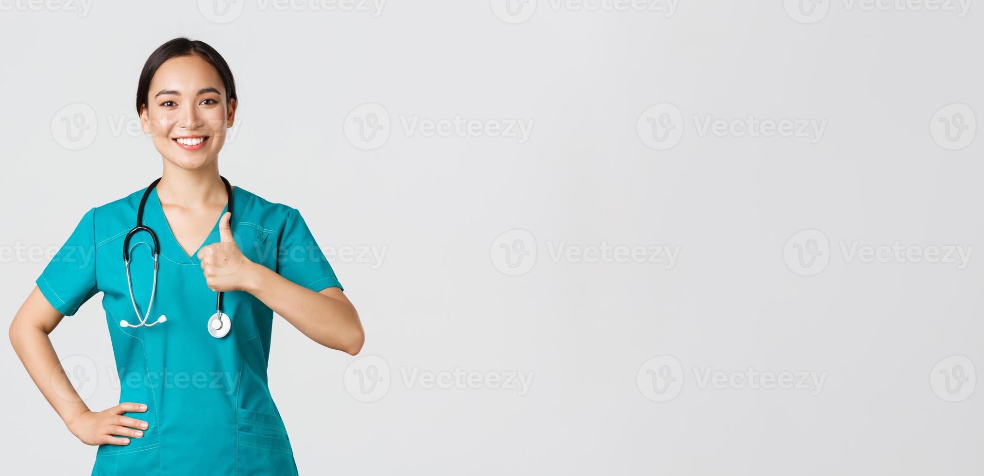 Covid-19, healthcare workers, pandemic concept. Smiling upbeat, confident female asian nurse in scrubs have all under control, show thumbs-up in approval, guarantee quality of service in clinic photo