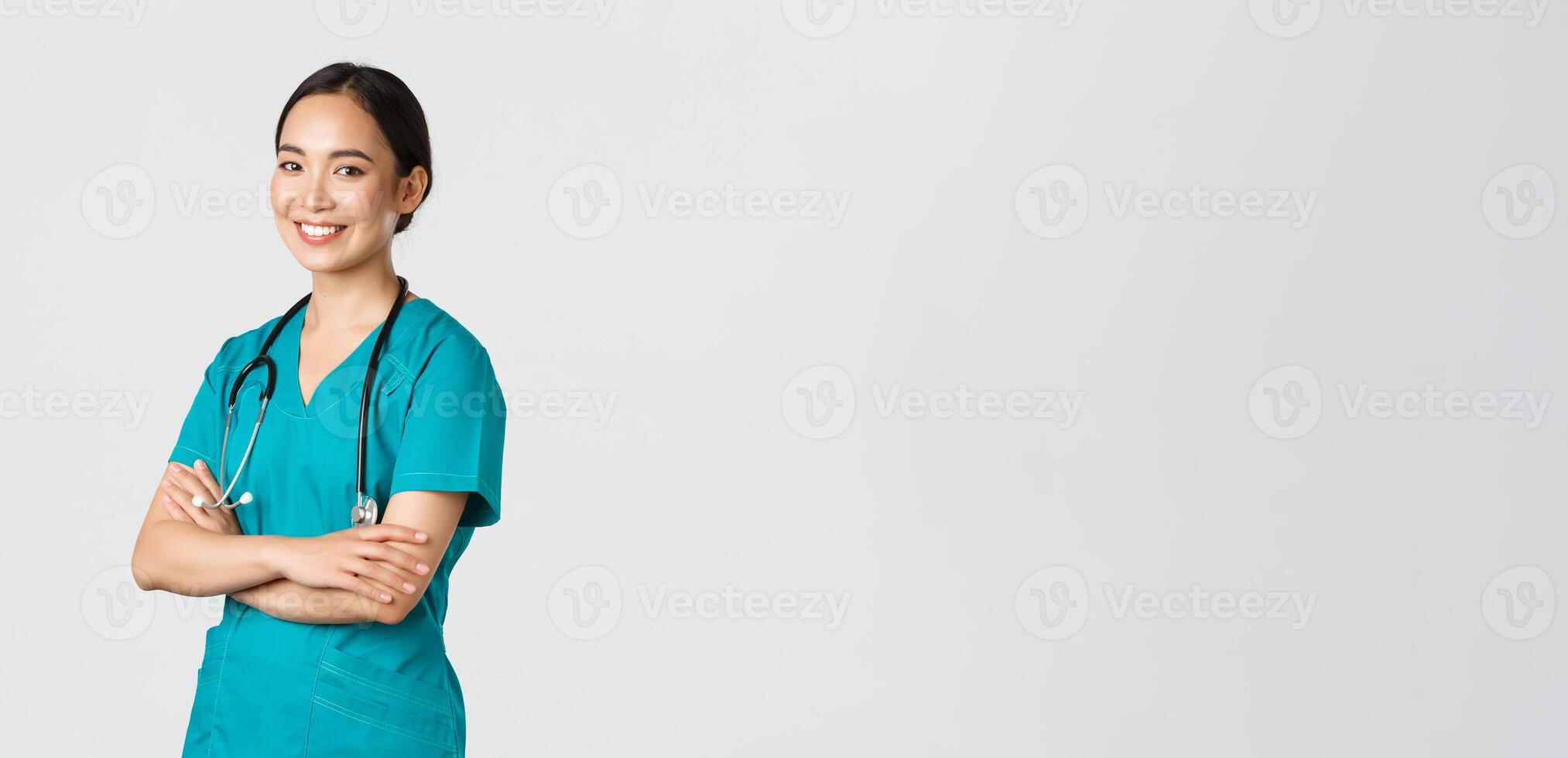 Covid-19, healthcare workers, pandemic concept. Professional confident, smiling asian female doctor, nurse in scrubs with stethoscope for examinations, cross arms and look at camera photo