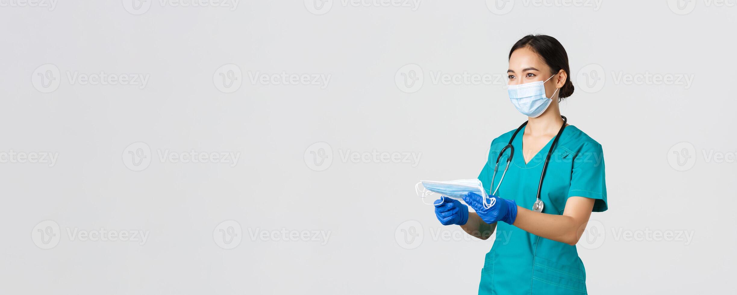 Covid-19, coronavirus disease, healthcare workers concept. Smiling friendly female nurse, physician in scrubs and rubber gloves provide patients with medical masks, white background photo
