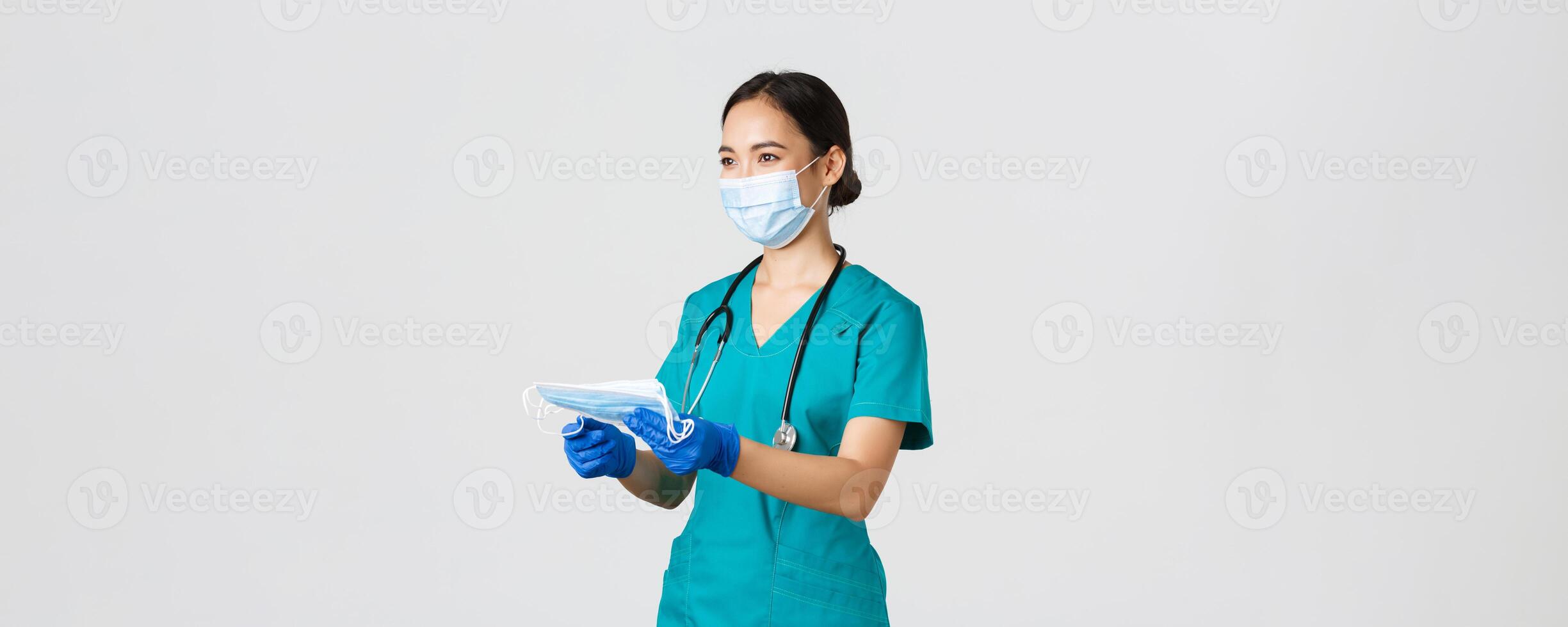 Covid-19, coronavirus disease, healthcare workers concept. Smiling friendly female nurse, physician in scrubs and rubber gloves provide patients with medical masks, white background photo