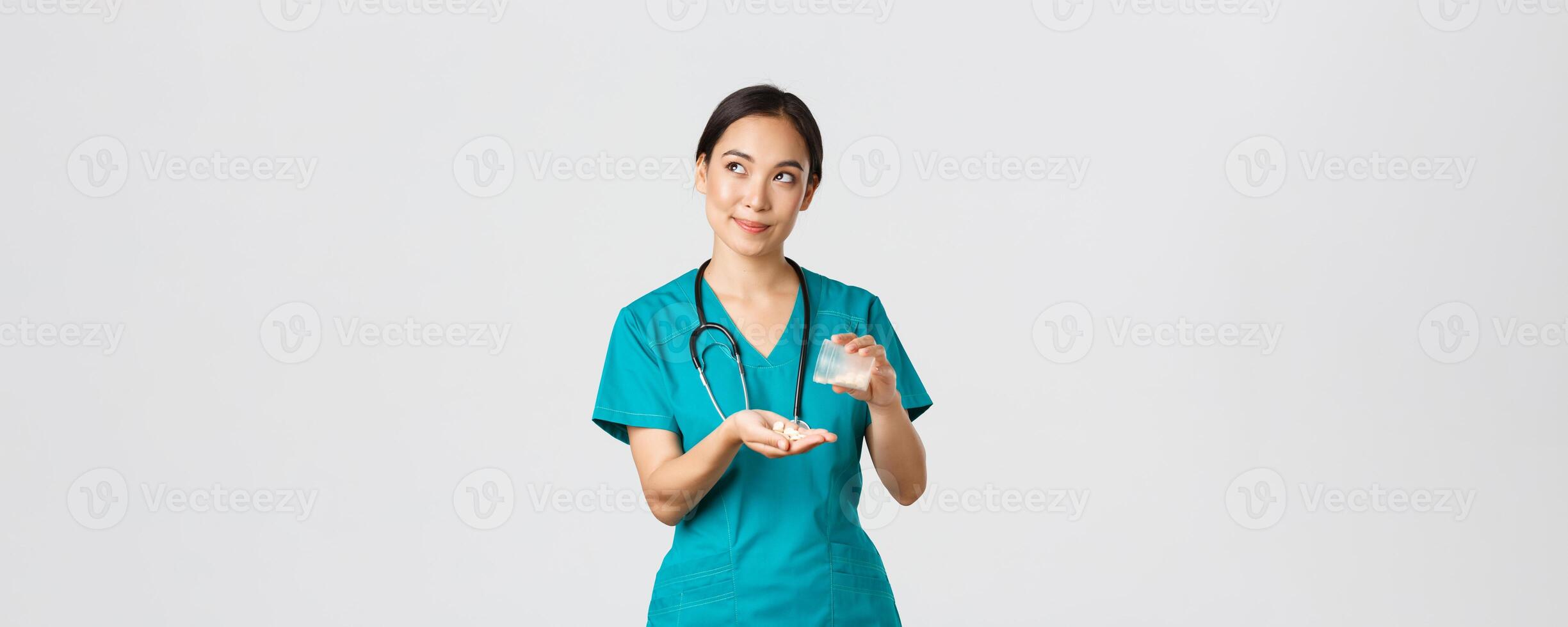 Healthcare workers, preventing virus, quarantine campaign concept. Thoughtful and caring smiling asian female nurse, intern in scrubs handle medication to patient and looking dreamy upper left corner photo