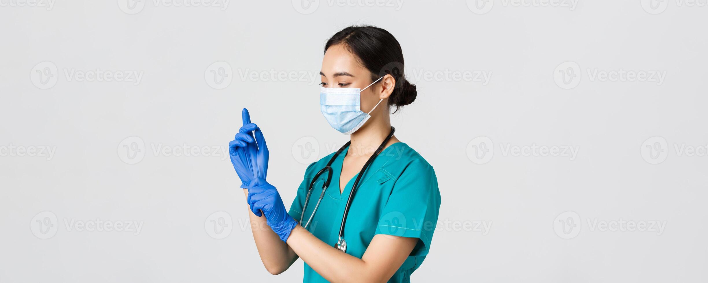 Covid-19, coronavirus disease, healthcare workers concept. Professional smiling asian female nurse, physician in scrubs and medical mask put on rubber gloves for checkup, patient examination photo