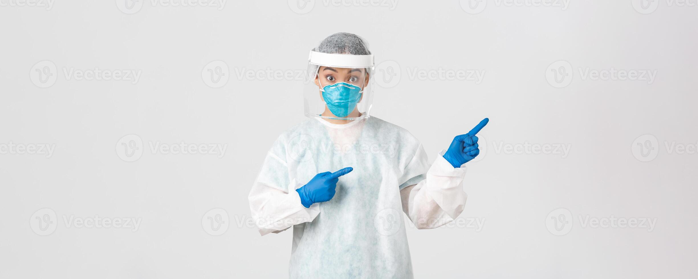 Covid-19, coronavirus disease, healthcare workers concept. Surprised and intrigued asian female doctor, tech lab employee in personal protective equipment look amazed and pointing fingers right photo