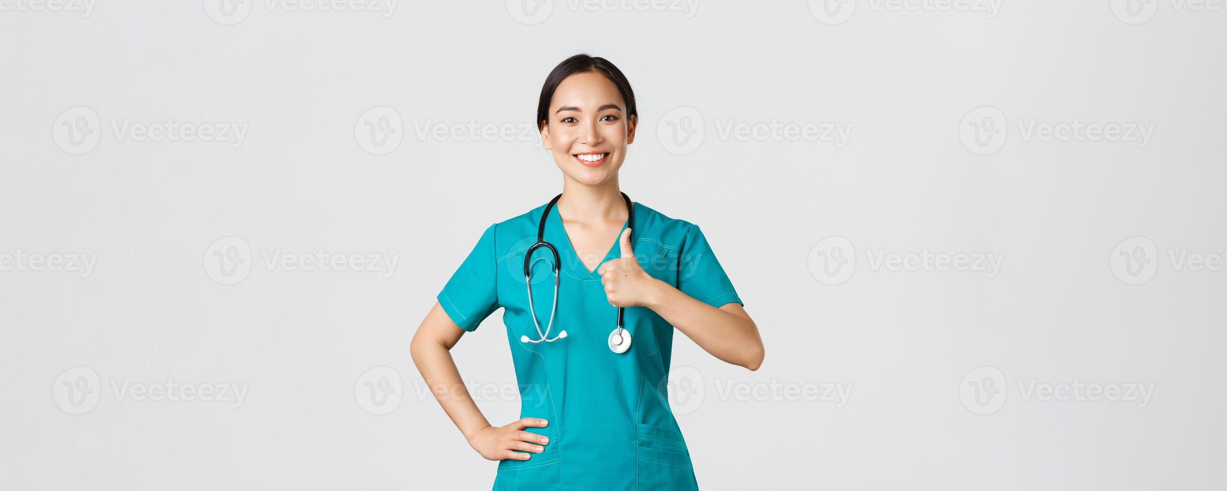 Covid-19, healthcare workers, pandemic concept. Smiling upbeat, confident female asian nurse in scrubs have all under control, show thumbs-up in approval, guarantee quality of service in clinic photo