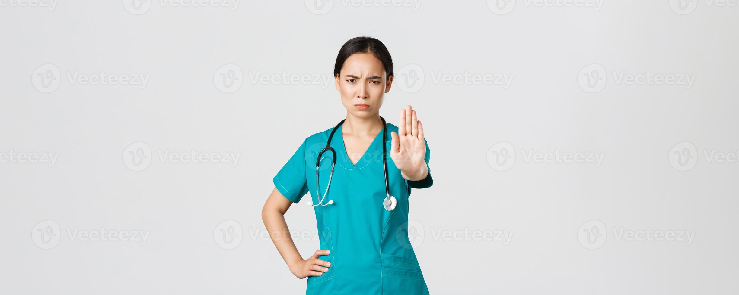 Covid-19, healthcare workers, pandemic concept. Angry serious-looking asian doctor, female physician or nurse in scrubs frowning displeased, extend hand to show stop, disagree, prohibit or forbid photo