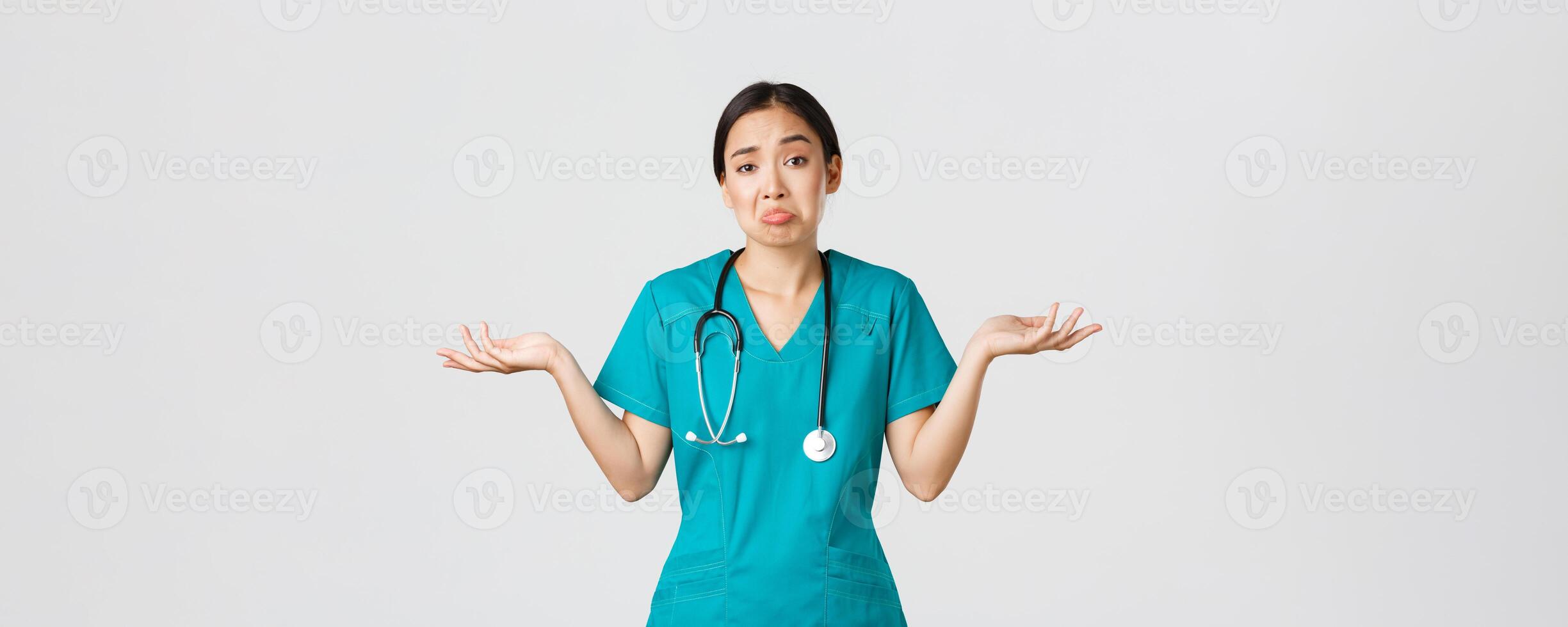 Covid-19, healthcare workers, pandemic concept. Portrait of clueless asian female nurse, woman doctor shrugging and spread hands sideways unaware, dont know, cant help, white background photo