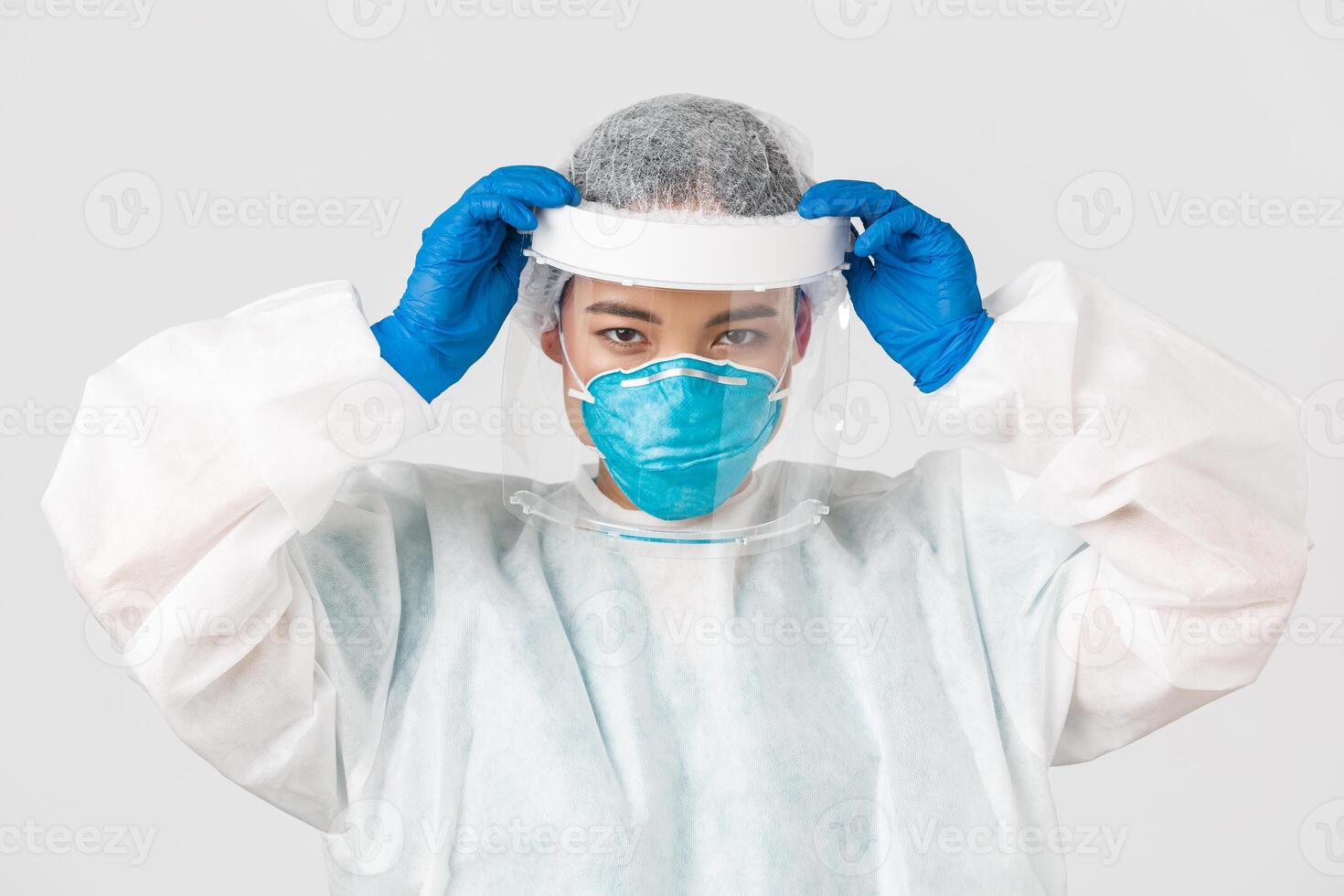 Covid-19, coronavirus disease, healthcare workers concept. Confident serious-looking asian female doctor, put on face shield and personal protective equipment before entering contagious zone photo