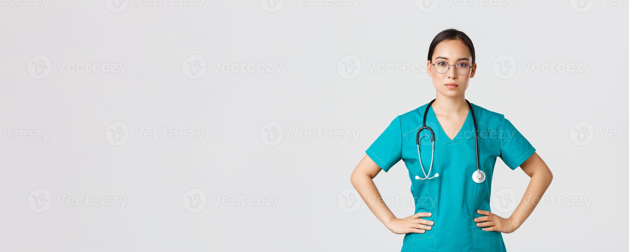 Covid-19, healthcare workers, pandemic concept. Confident determined asian female nurse helping patients, working with coronavirus disease, looking ready, wearing scrubs and glasses, white background photo