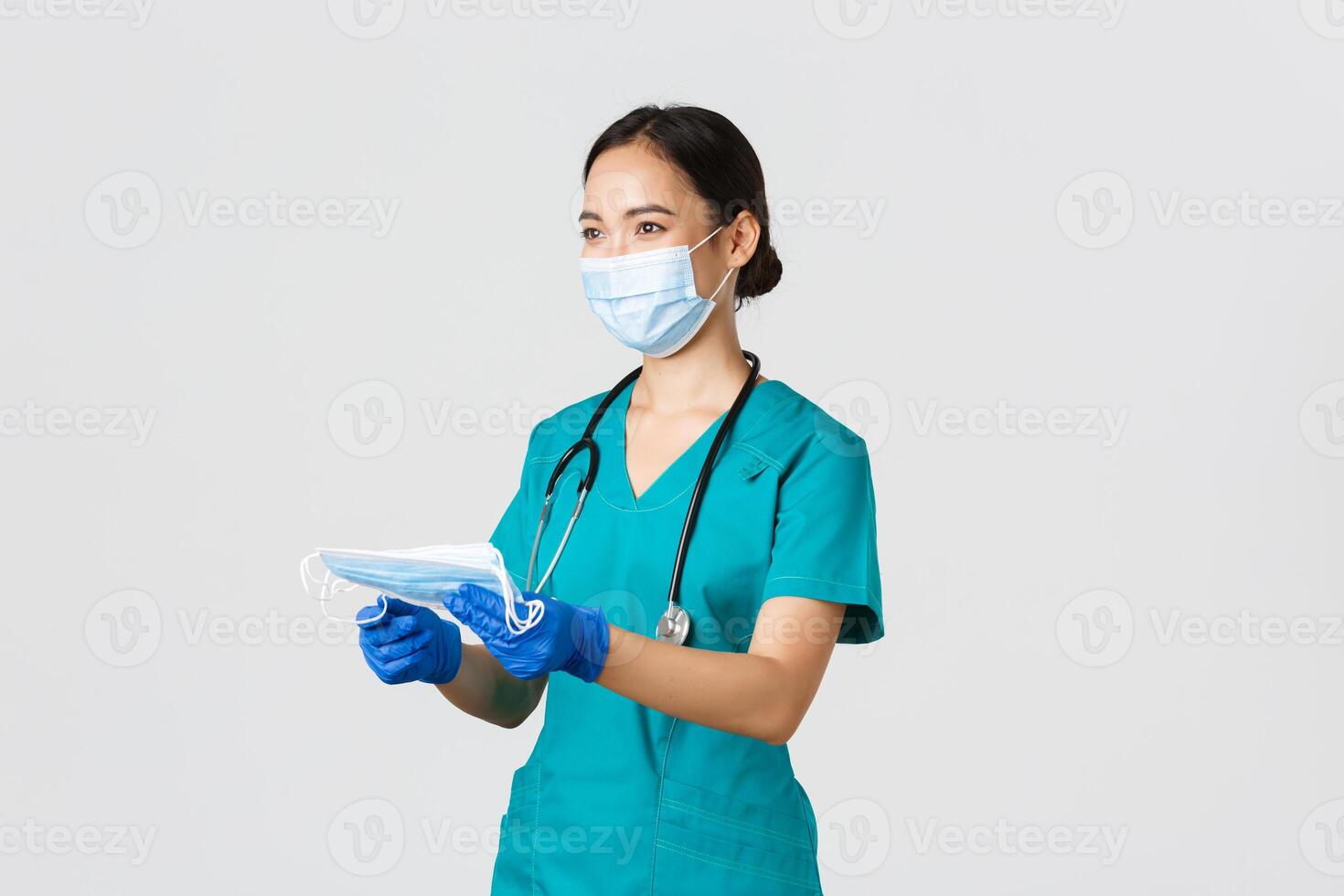 Covid-19, coronavirus disease, healthcare workers concept. Smiling friendly female nurse, physician in scrubs and rubber gloves provide patients with medical masks, white background photo