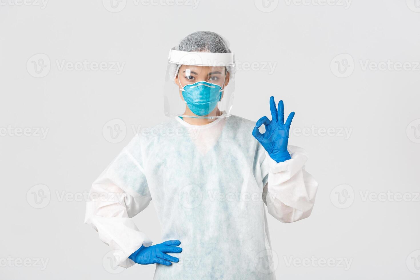 Covid-19, coronavirus disease, healthcare workers concept. Serious-looking professional female asian doctor in personal protective equipment, showing okay gesture, ensure safety of patient photo