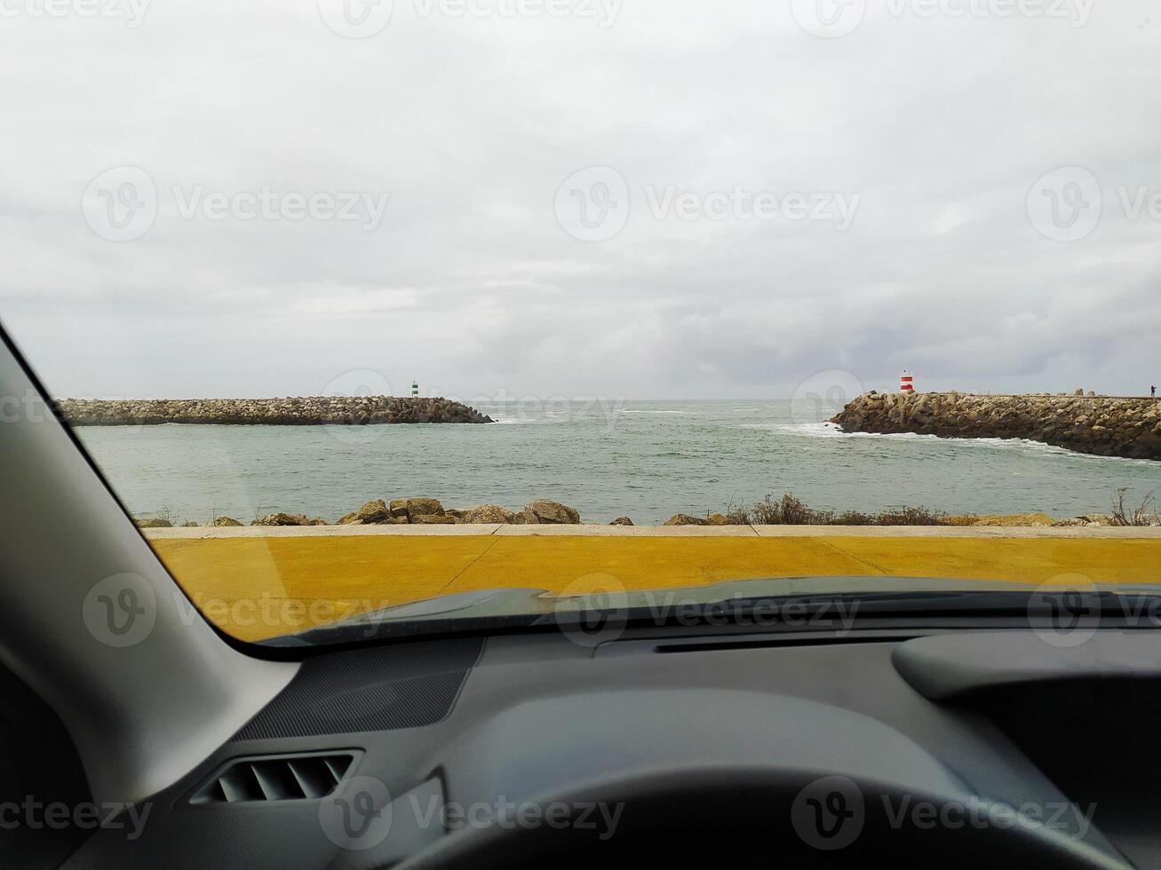 Sea view from the car interior. Lighthouse and ocean pier through the steering wheel photo