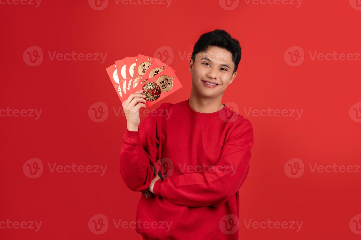 Smiling handsome Asian man holding red Ang Pao in studio isolated red background for Chinese new year concepts photo