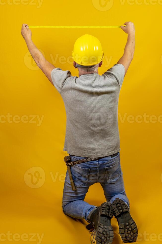 craftsman worker with hard hat is measuring with a tape measure isolated on yellow background photo