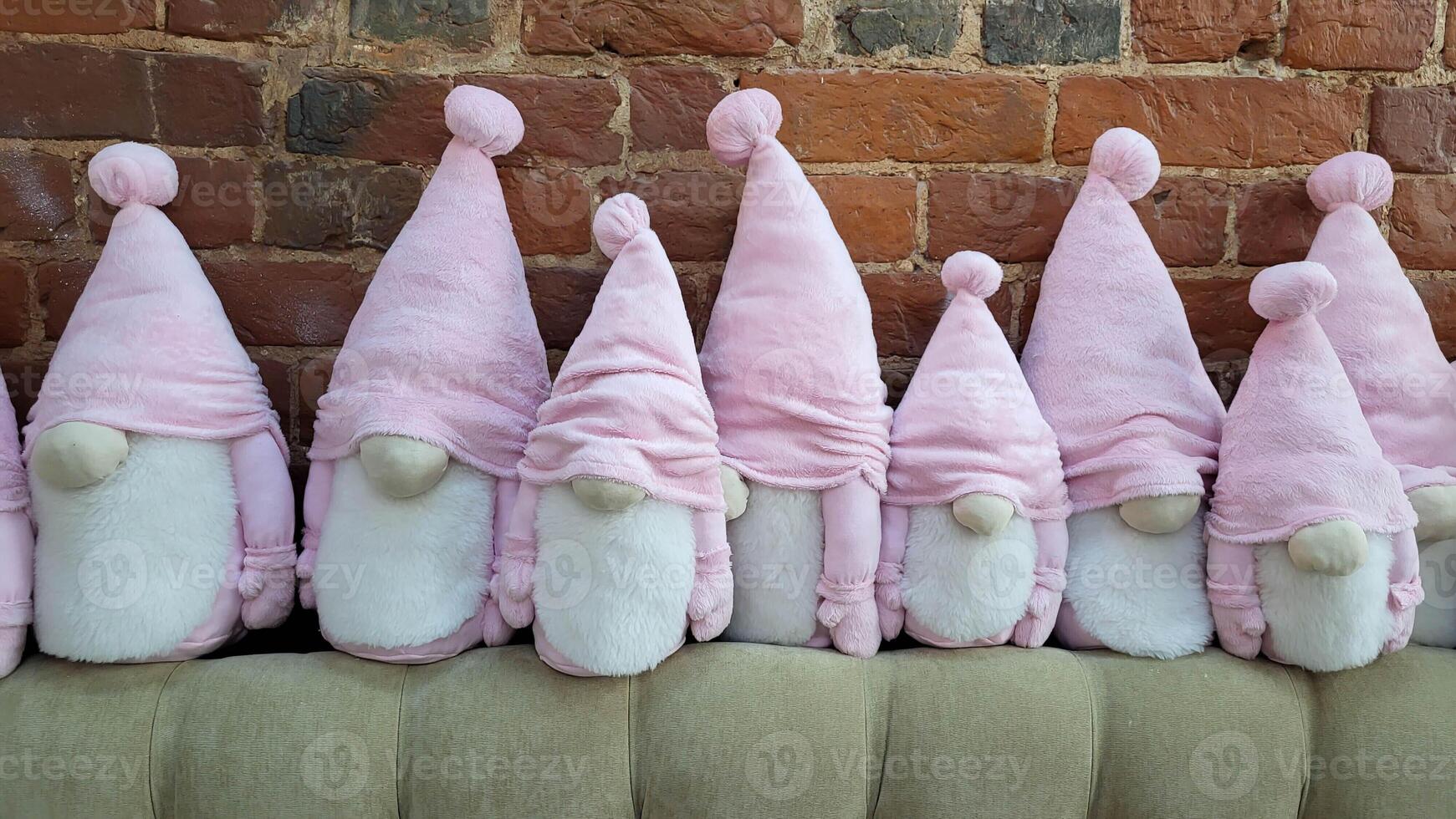 A cute family of bearded dwarfs in pink hats sits against a brick wall photo