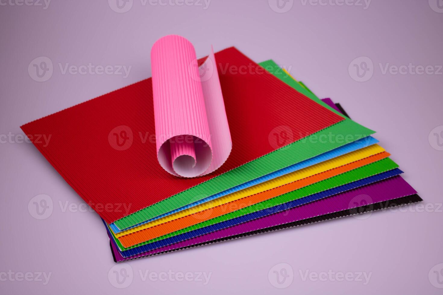 A roll of pink corrugated paper on multicolored leaves of corrugated paper photo