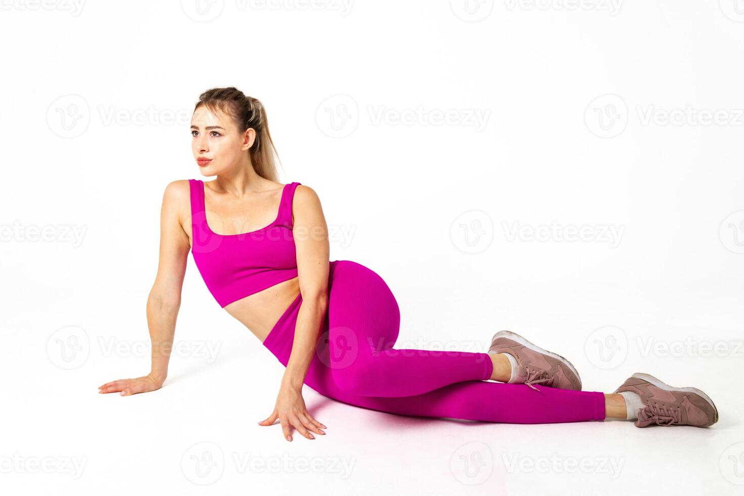 mujer en vibrante rosado Deportes atuendo acostado en piso con uno pierna doblado mirando lejos foto
