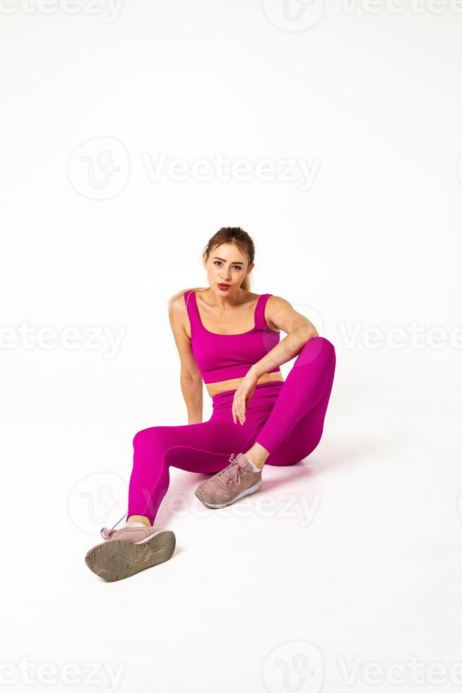 Woman in vibrant pink sports outfit sitting on floor with one leg bent photo