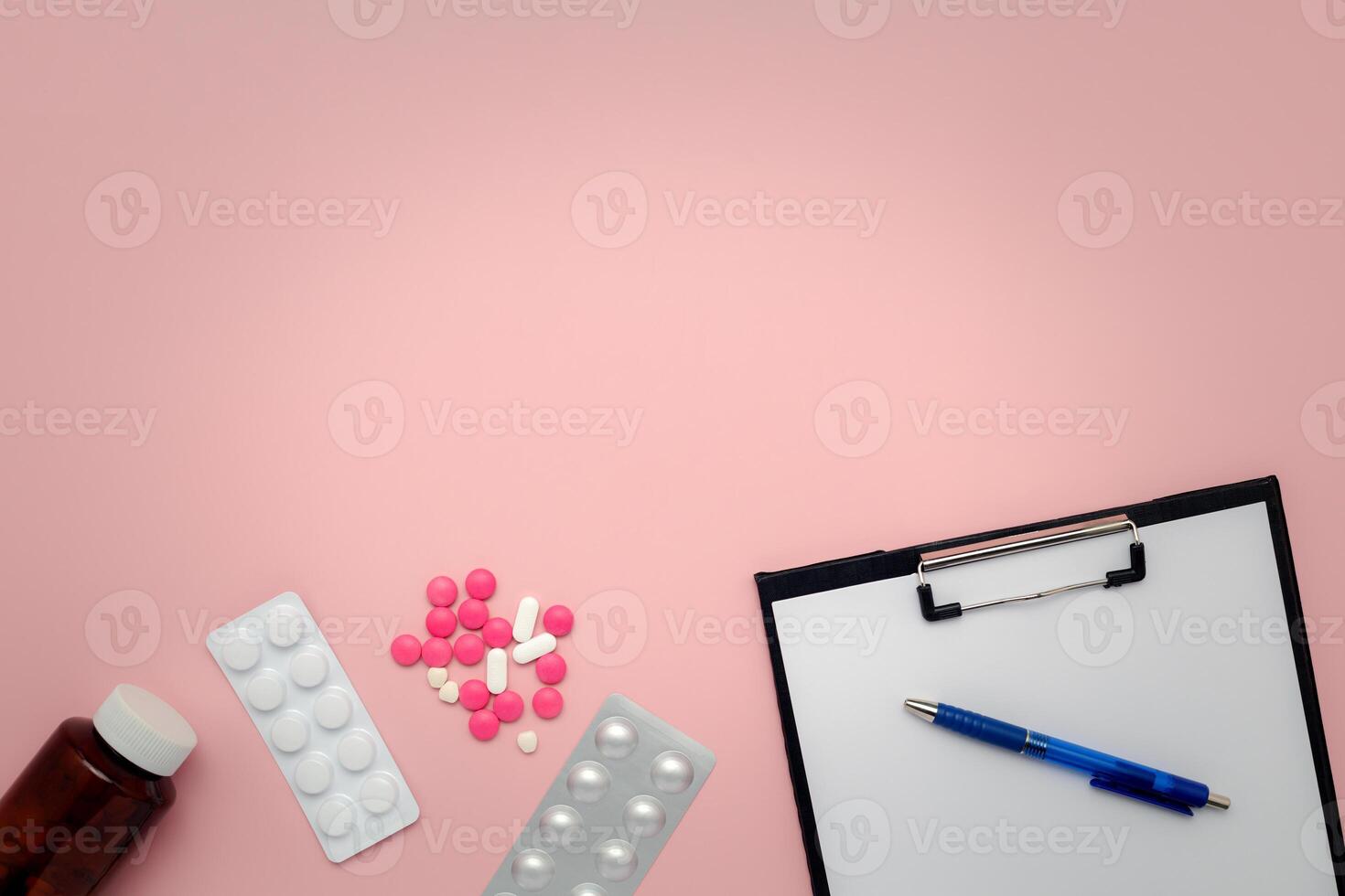 A bottle of medicine, medication blister packs, pills, clipboard and pen on a pink background photo