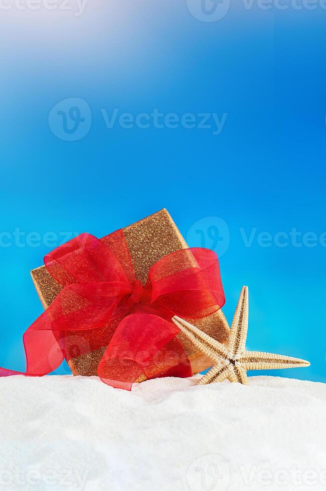 dorado regalo caja con rojo arco y estrella de mar en playa. 8vo de marzo, internacional De las mujeres y las madres día, cumpleaños, Navidad, nuevo año, boda, enamorado. Copiar espacio foto