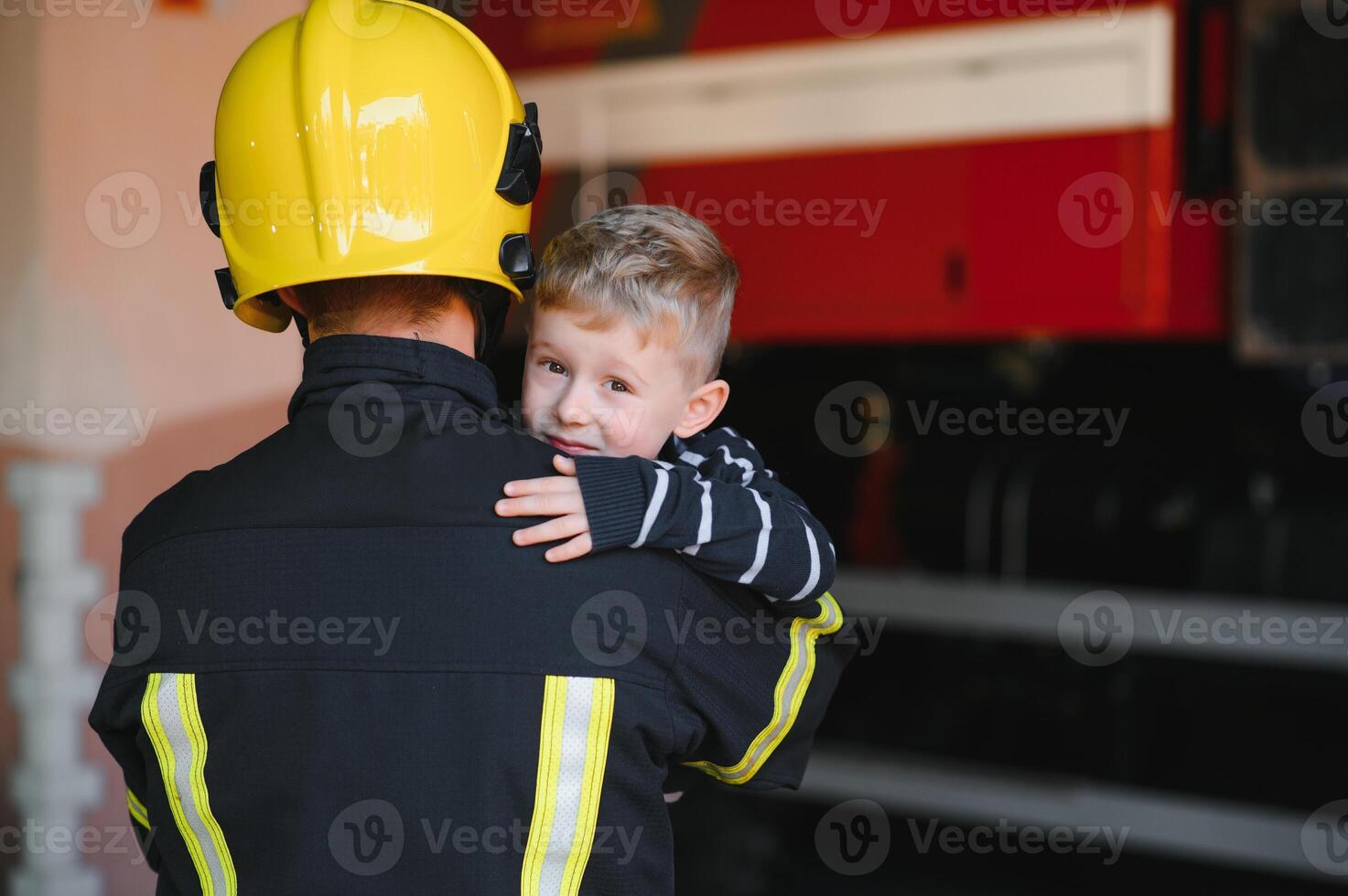 Dirty firefighter in uniform holding little saved boy standing on black background. photo