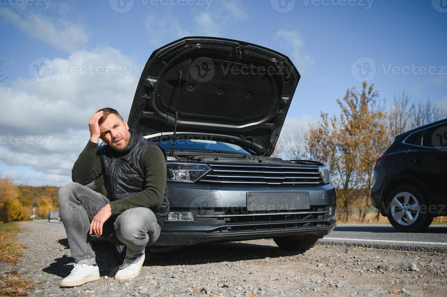 Man repairing a broken car by the road. Man having trouble with his broken car on the highway roadside. Man looking under the car hood. Car breaks down on the autobahn. Roadside assistance concept. photo