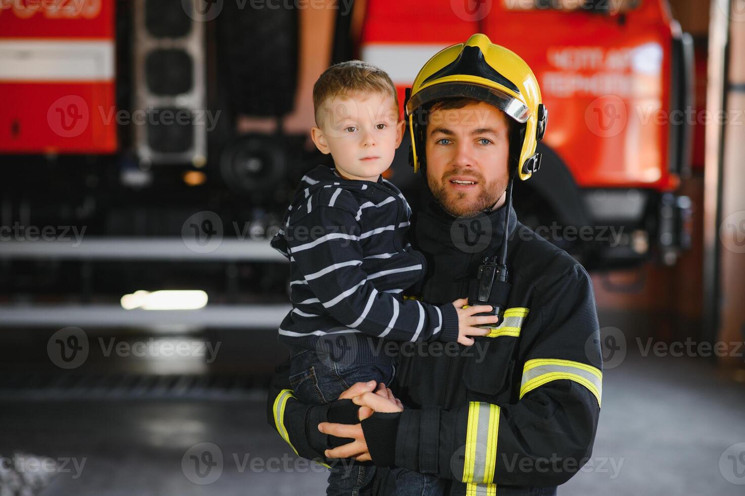 A firefighter take a little child boy to save him. Fire engine car on background. Fireman with kid in his arms. Protection concept. photo