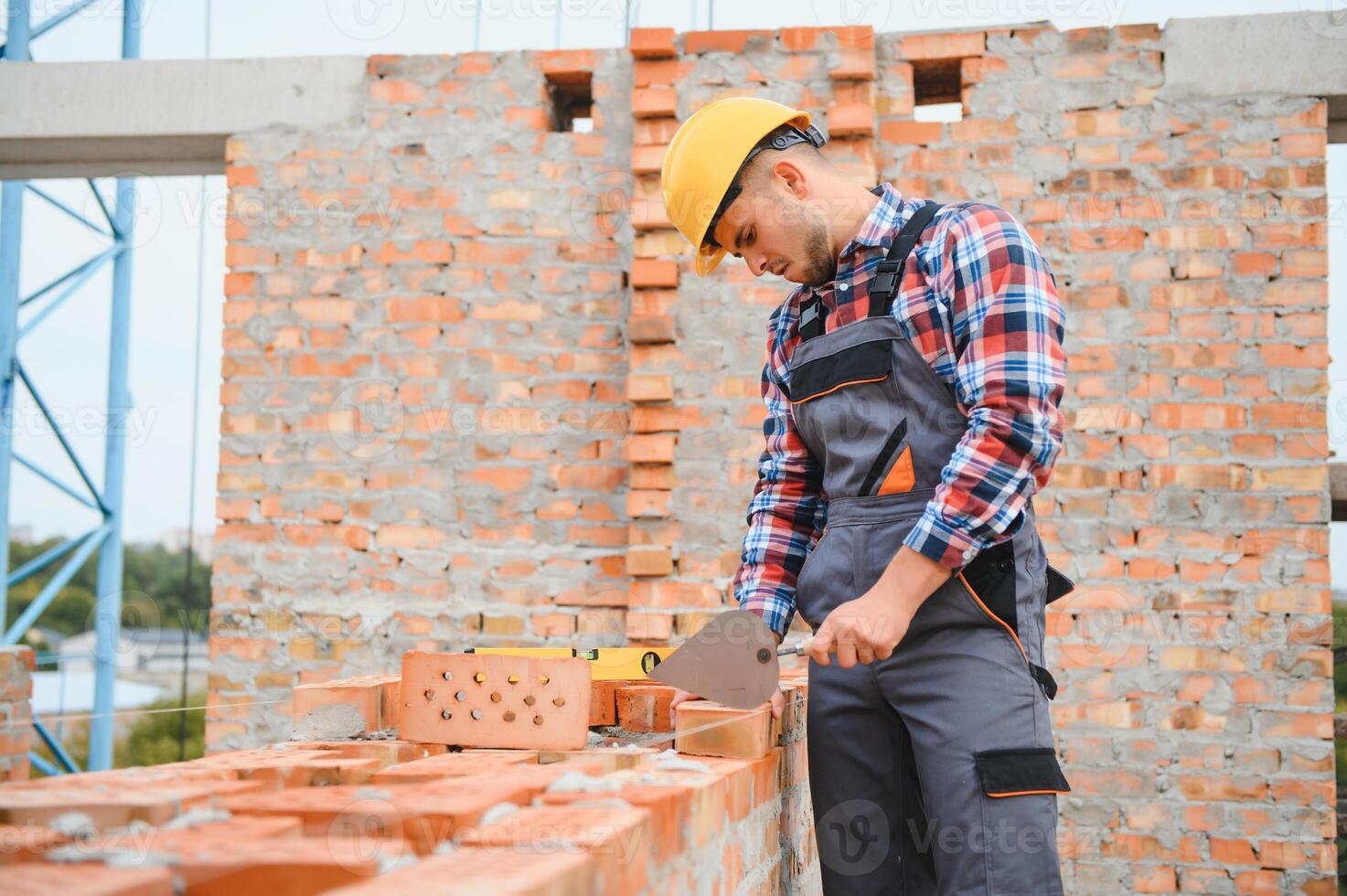 Using bricks. Young construction worker in uniform is busy at the unfinished building photo