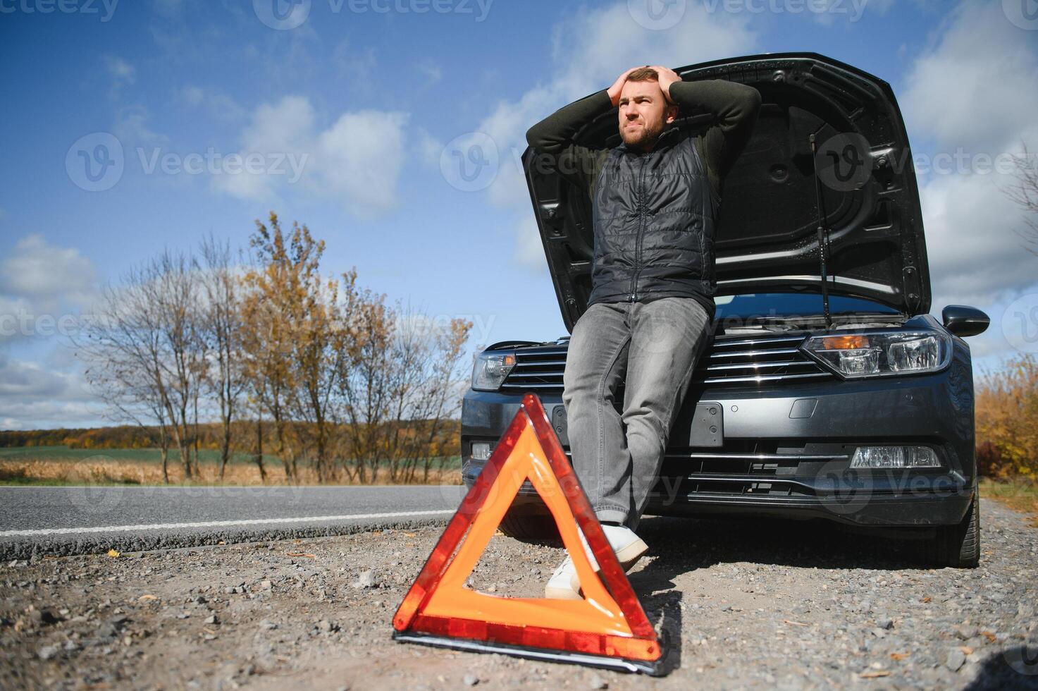 Man repairing a broken car by the road. Man having trouble with his broken car on the highway roadside. Man looking under the car hood. Car breaks down on the autobahn. Roadside assistance concept. photo