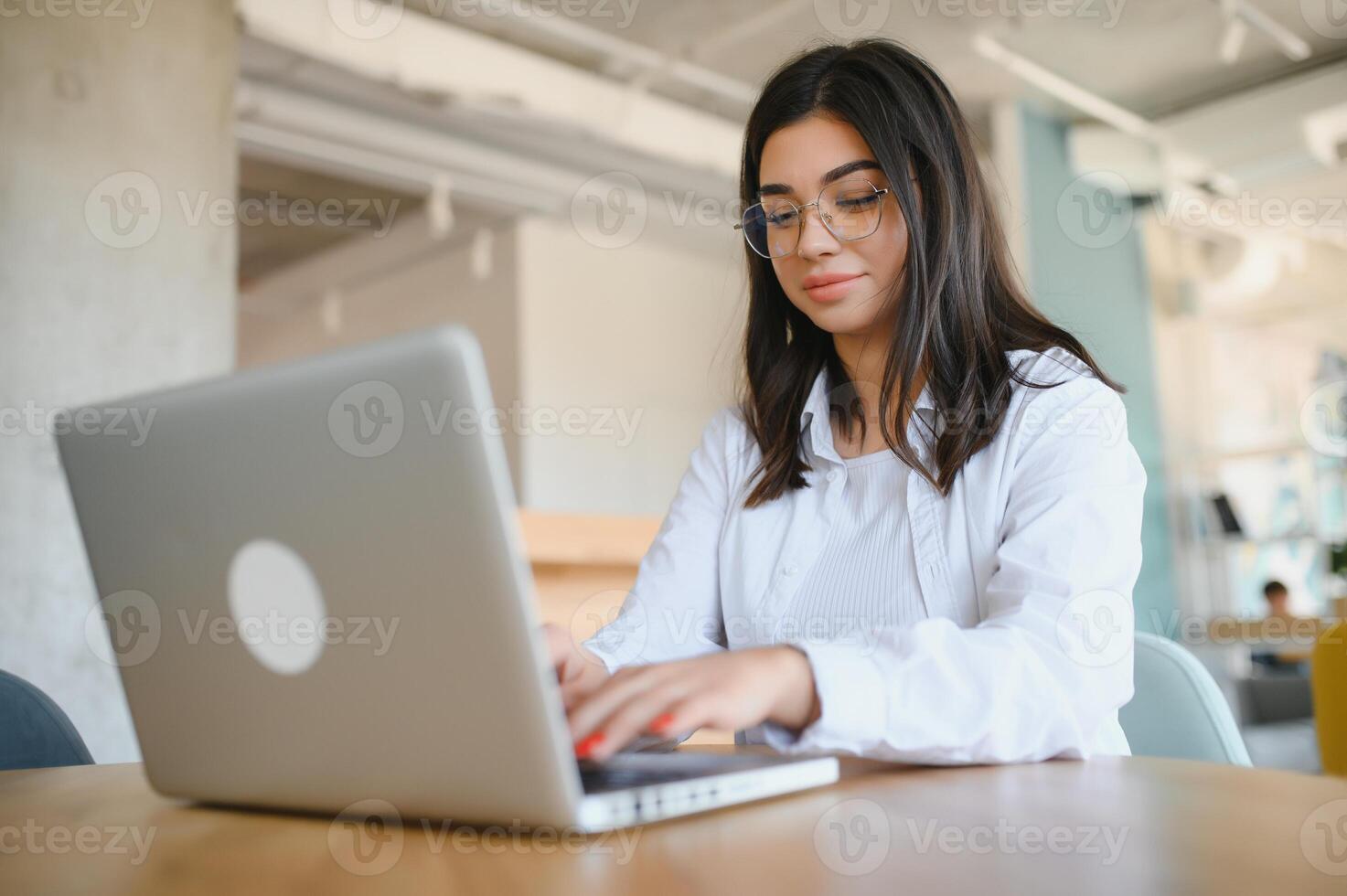 Beautiful Young Freelancer Woman Using Laptop Computer Sitting At Cafe Table. Happy Smiling Girl Working Online Or Studying And Learning While Using Notebook. Freelance Work, Business People Concept. photo