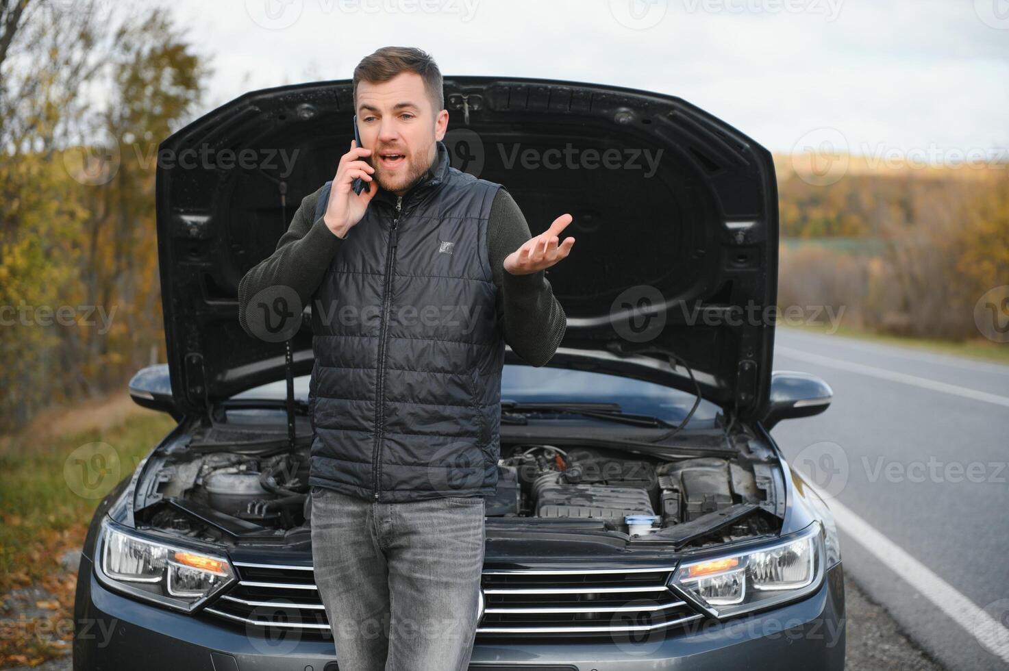 Handsome young man calling for assistance with his car broken down by the roadside photo