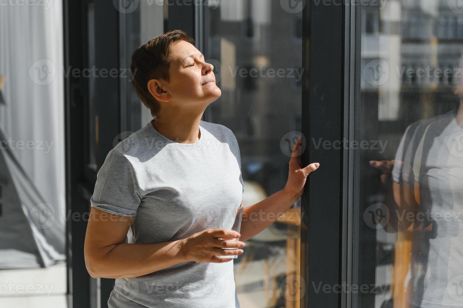 maduro mujer beber. medio años hembra en casual ropa tiene Fresco agua con limón jugo en sofá a hogar. concepto de sano dieta foto