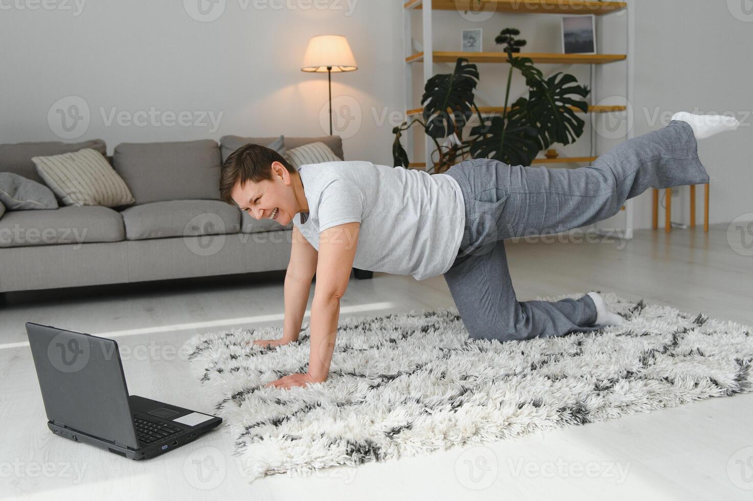 Middle aged woman in plank position keeps fit in her home - Elderly person has fun doing sports - mental and physical well-being concept photo