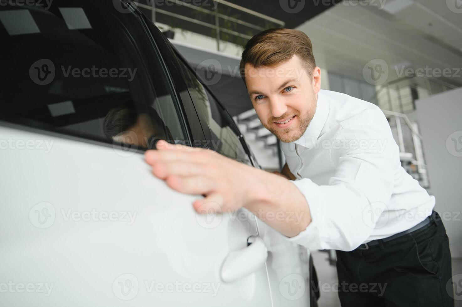 Visiting car dealership. Handsome bearded man is stroking his new car and smiling. photo