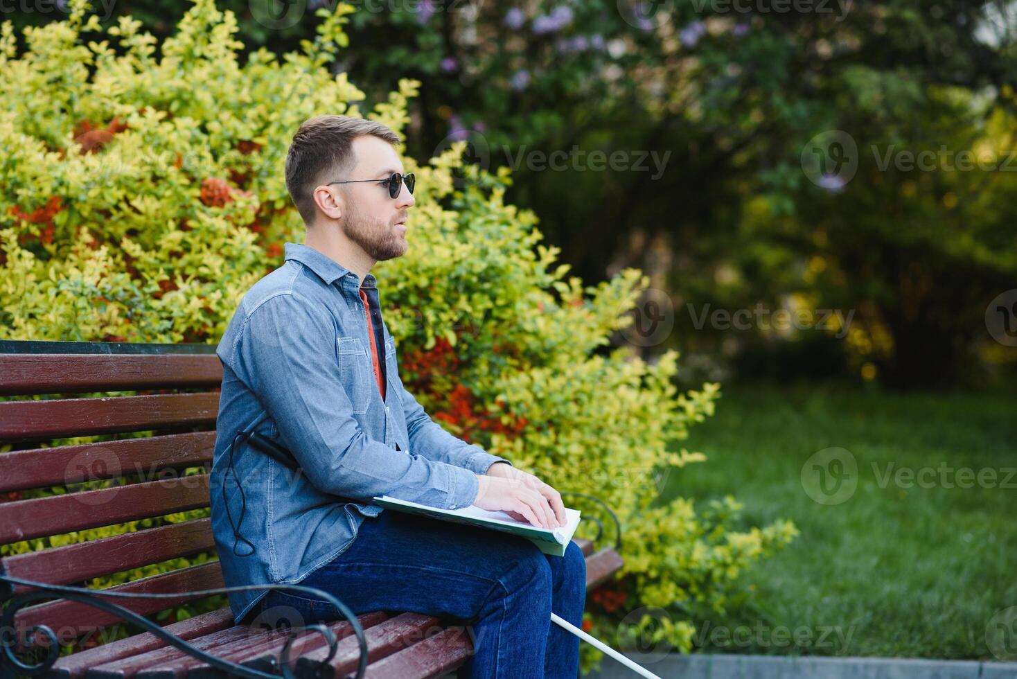 Blind man reading book on bench in park photo