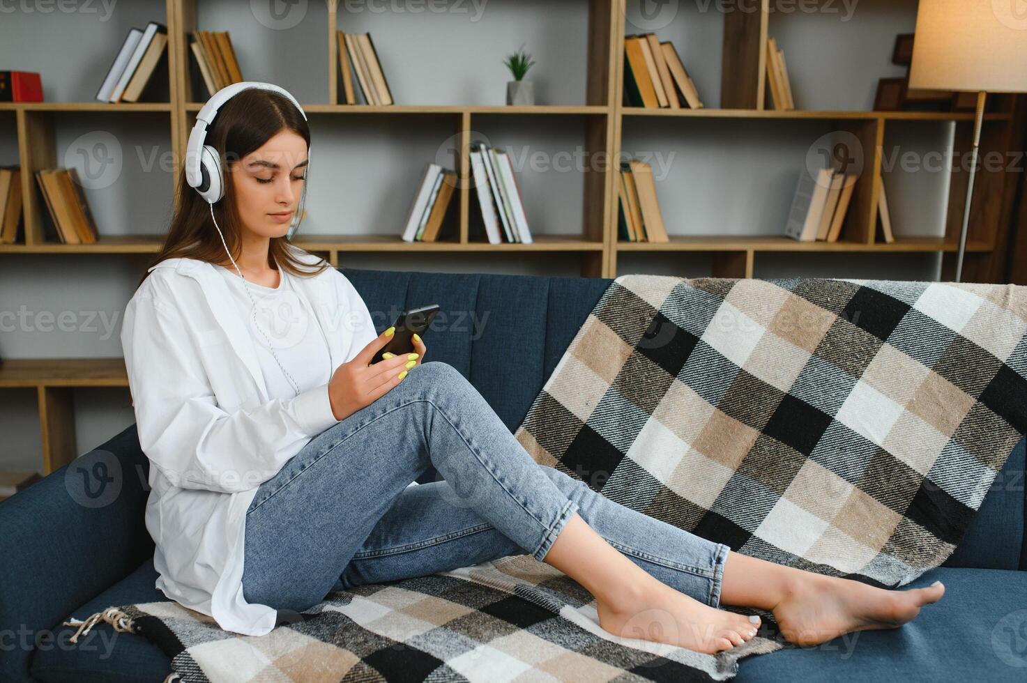 Portrait of attractive girl 20s wearing headphones using smartphone and listening to music while sitting on sofa at home photo