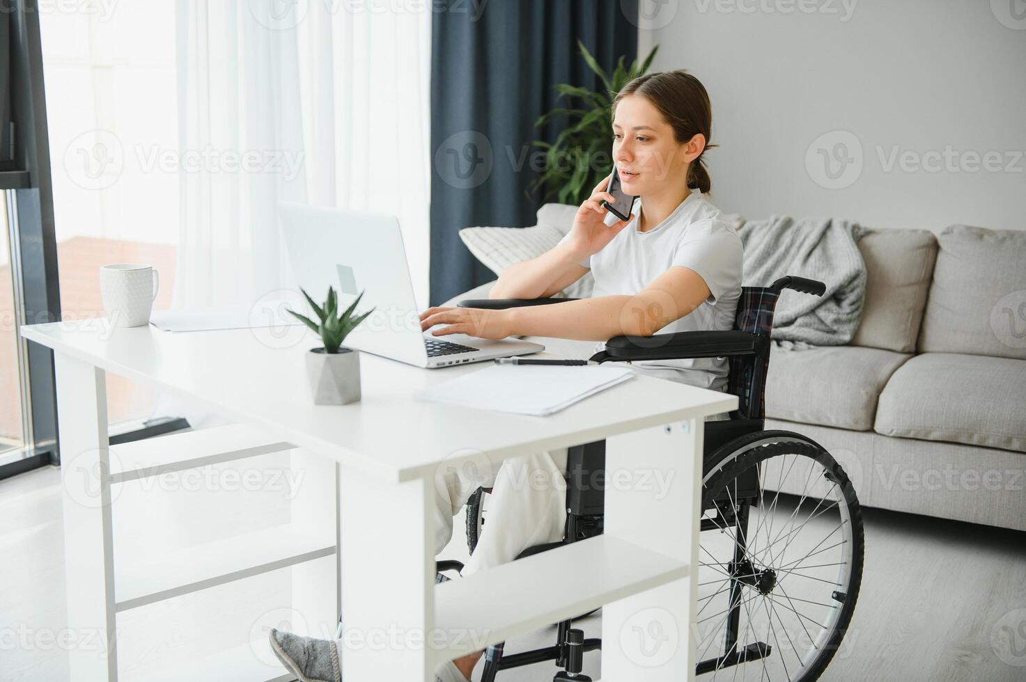 Female freelance programmer sitting in wheelchair and using computers while coding web game at home. photo