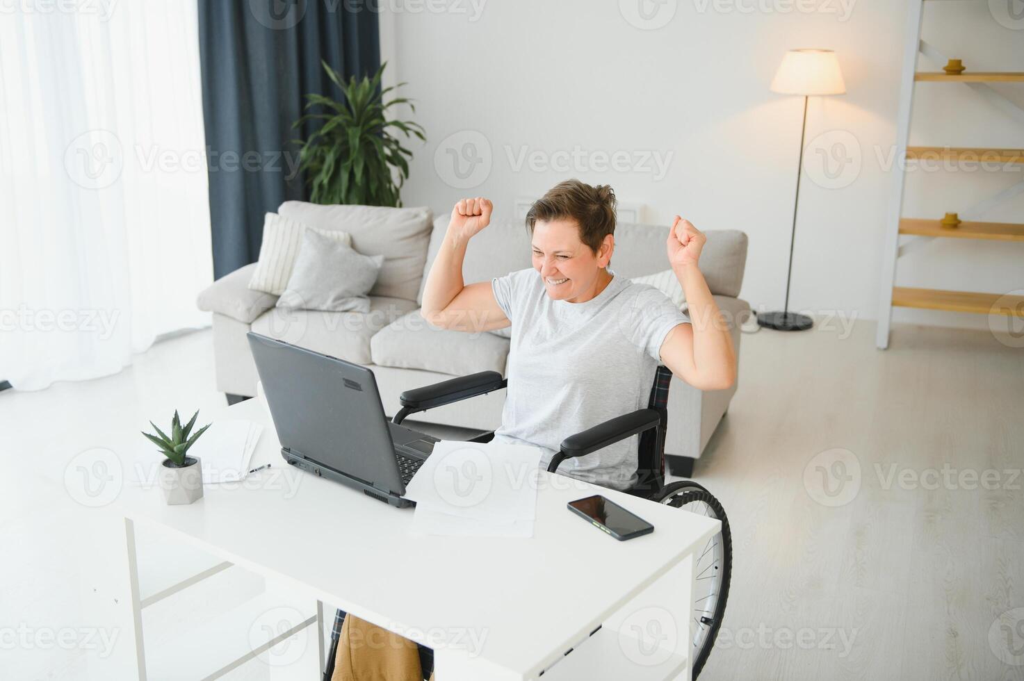 Positive elderly woman in wheelchair working on laptop, IT freelancer, online photo
