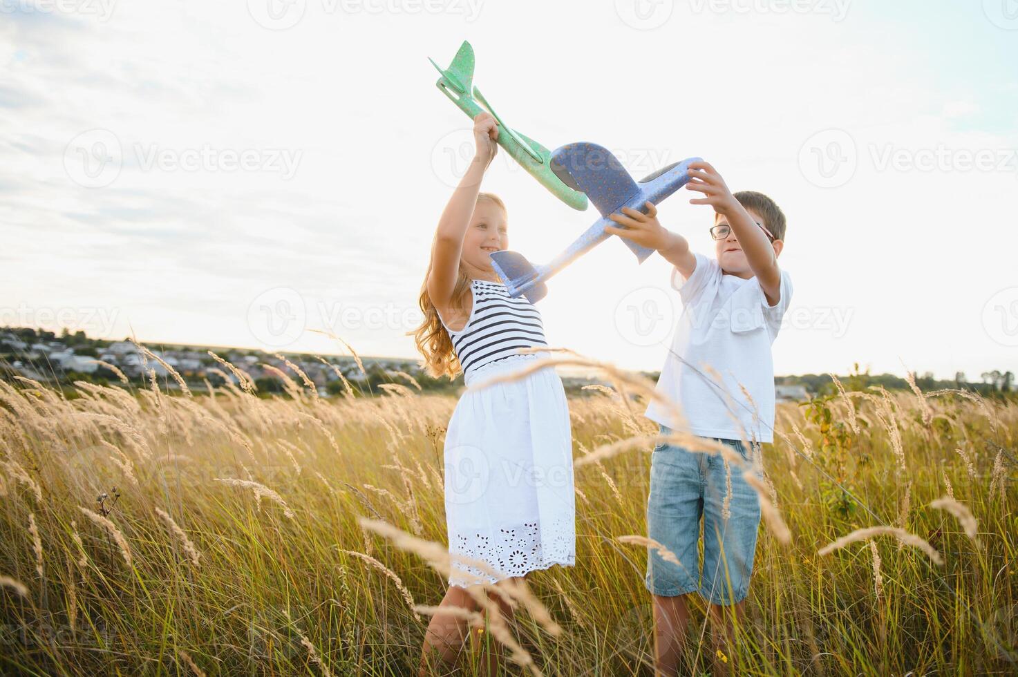Running boy and girl holding two green and blue airplanes toy in the field during summer sunny day photo