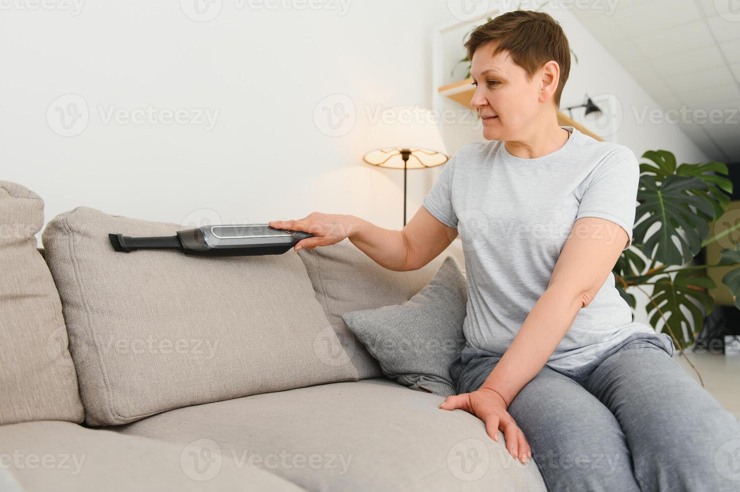 Portrait of senior woman with vacuum cleaner indoors at home, hoovering photo