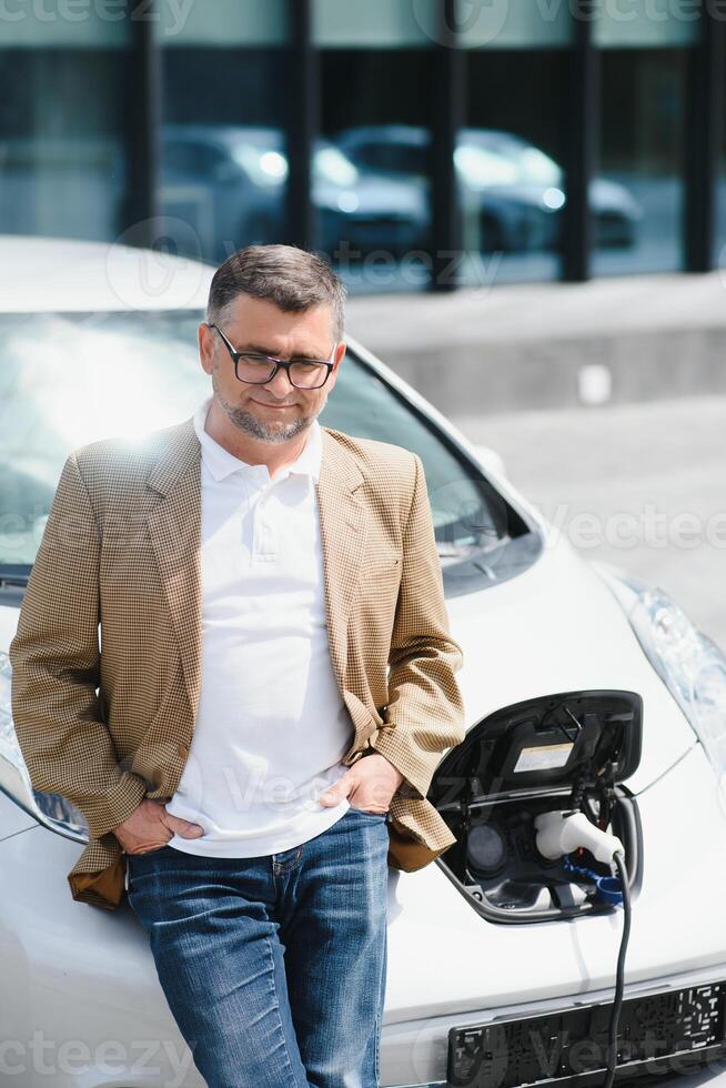 Casual man near electric car waiting for the finish of the battery charging process. photo